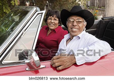 Stock Image - Hispanic couple smiling in convertible. Fotosearch