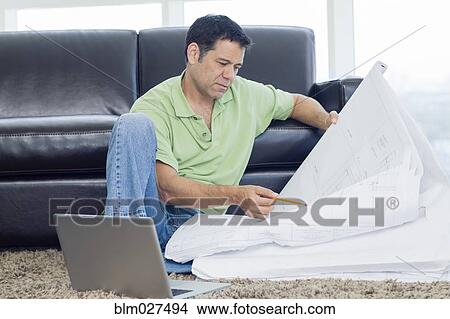 Picture - Hispanic man examining blueprints in living room. Fotosearch