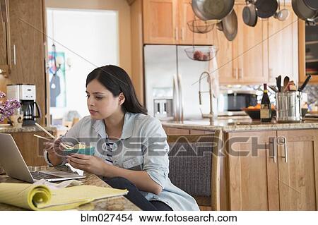 Picture - Hispanic woman eating Chinese food in kitchen. Fotosearch