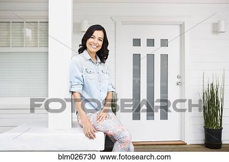 Stock Image - Hispanic woman smiling on front porch. Fotosearch
