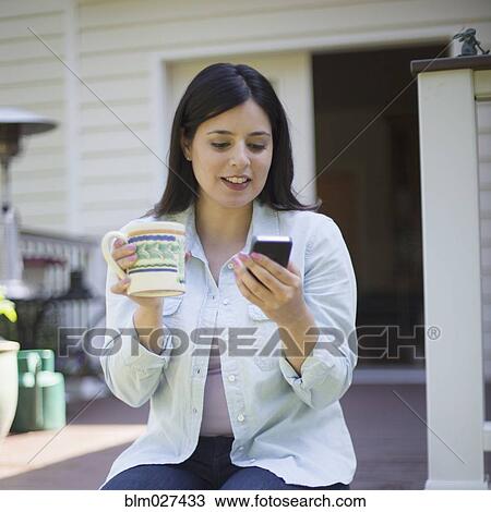 Stock Image - Hispanic woman using cell phone on deck. Fotosearch