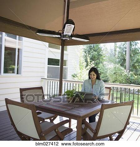 Stock Image - Hispanic woman using laptop at table on patio. Fotosearch