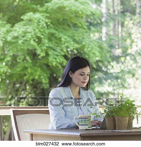 Stock Image - Hispanic woman using laptop on patio. Fotosearch