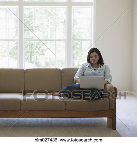 Stock Photograph - Hispanic woman using laptop on sofa. Fotosearch