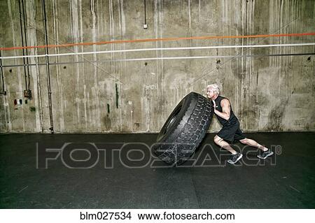 Picture - Mixed race man pushing large tire in gym. Fotosearch