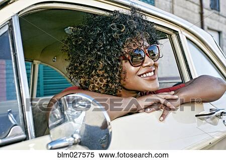 Stock Photography - Mixed race woman sitting in vintage car. Fotosearch