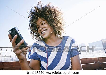 Stock Image - Mixed race woman using cell phone. Fotosearch