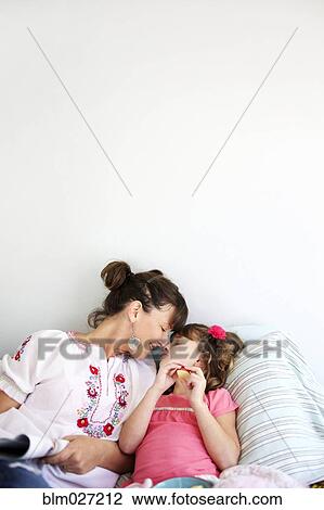 Stock Image - Mother and daughter relaxing on bed. Fotosearch