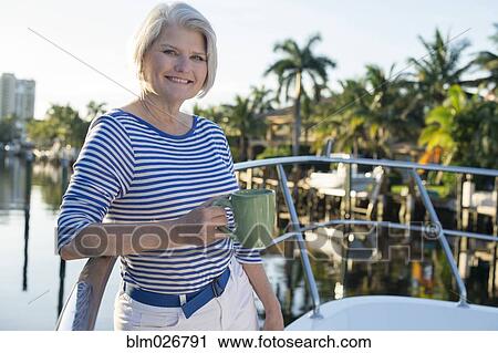Stock Image - Older Caucasian woman having coffee on boat deck. Fotosearch