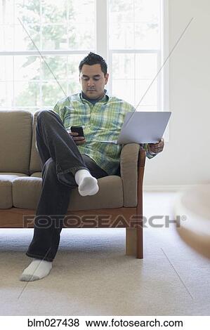 Stock Photo - Pacific Islander man using laptop and cell phone. Fotosearch