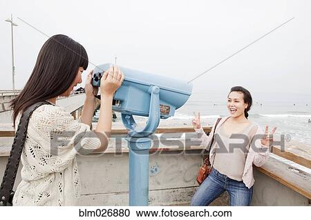 Stock Image - Women playing with telescope at beach. Fotosearch