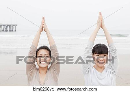 Stock Photography - Women practicing yoga on beach. Fotosearch
