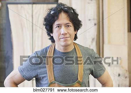 Stock Image - Asian carpenter standing in workshop. Fotosearch