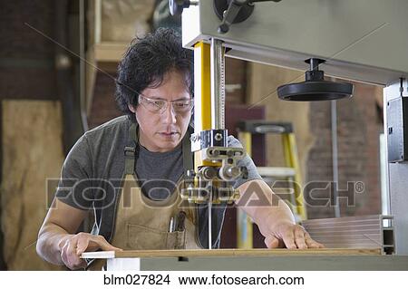 Picture - Asian carpenter using cutting machine in workshop. Fotosearch