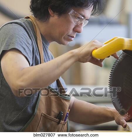 Stock Photo - Asian carpenter using saw in workshop. Fotosearch