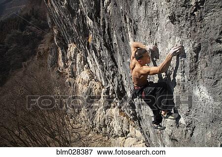 Asian climber scaling steep cliff face View Large Photo Image Stock Photo - Asian climber scaling steep cliff face. Fotosearch