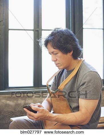 Stock Photo - Asian craftsman using cell phone in workshop. Fotosearch