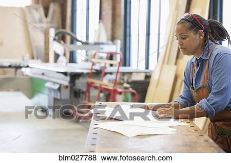 Stock Photo - Black carpenter looking at plan in workshop. Fotosearch