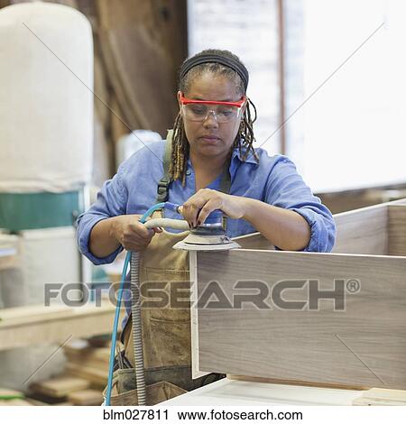 Stock Image - Black carpenter using sander in workshop. Fotosearch