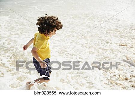 Stock Photography - Boy splashing in waves on beach. Fotosearch