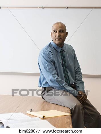 Stock Photo - Businessman sitting on desk in office. Fotosearch