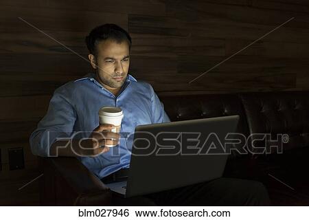 Stock Photograph - Businessman using laptop on sofa at night. Fotosearch