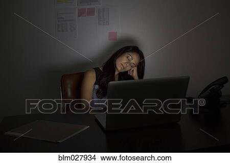 Picture - Businesswoman sleeping at desk at night. Fotosearch