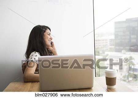 Stock Photograph - Businesswoman talking on cell phone at desk. Fotosearch
