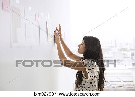 Businesswoman taping up papers on office wall View Large Photo Image Stock Photo - Businesswoman taping up papers on office wall. Fotosearch