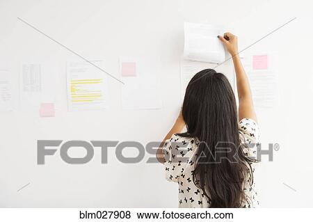 Stock Photo - Businesswoman taping up papers on office wall. Fotosearch