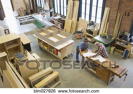 Stock Photograph - Carpenters reviewing blueprints in workshop. Fotosearch