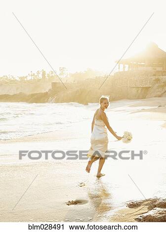 Stock Image - Caucasian bride holding bouquet on beach. Fotosearch