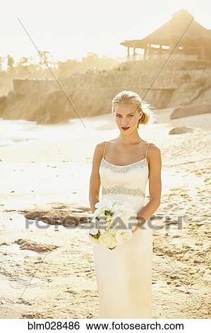 Stock Photograph - Caucasian bride holding bouquet on beach. Fotosearch