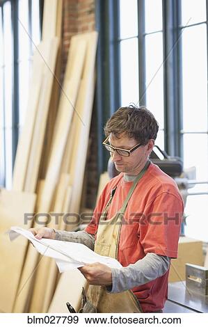 Stock Photo - Caucasian carpenter reviewing blueprint in workshop. Fotosearch