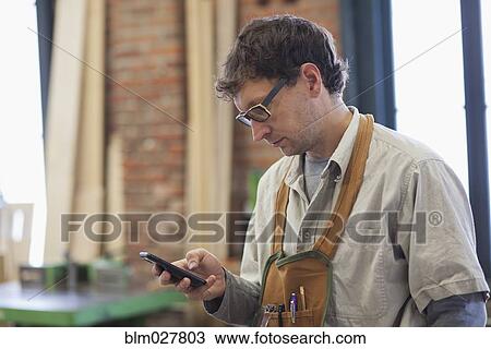 Caucasian carpenter using cell phone in workshop View Large Photo Image Stock Image - Caucasian carpenter using cell phone in workshop. Fotosearch