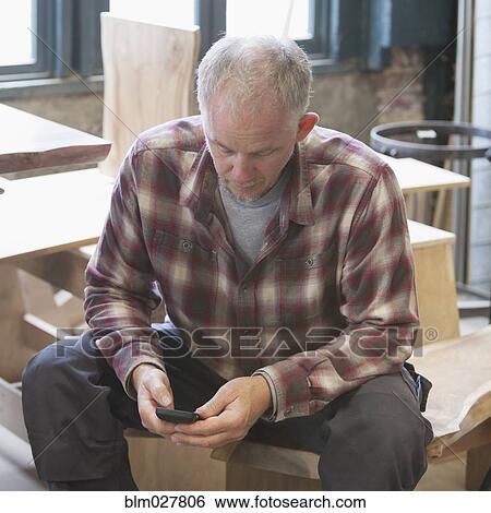 Stock Photograph - Caucasian carpenter using cell phone in workshop. Fotosearch