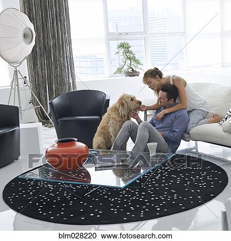 Stock Image - Caucasian couple petting dog in living room. Fotosearch