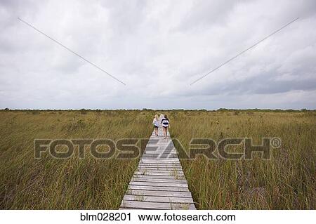 Stock Image - Caucasian girls on wooden walkway in rural landscape. Fotosearch
