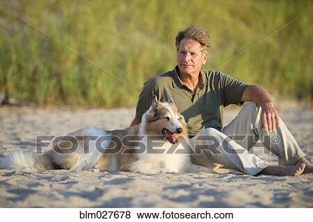 Caucasian man sitting with dog on beach View Large Photo Image Stock Photo - Caucasian man sitting with dog on beach. Fotosearch