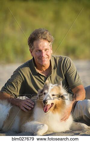 Caucasian man sitting with dog on beach View Large Photo Image Stock Photo - Caucasian man sitting with dog on beach. Fotosearch