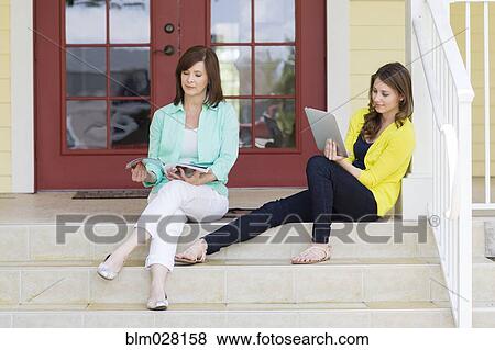 Stock Photo - Caucasian mother and daughter relaxing on front steps. Fotosearch