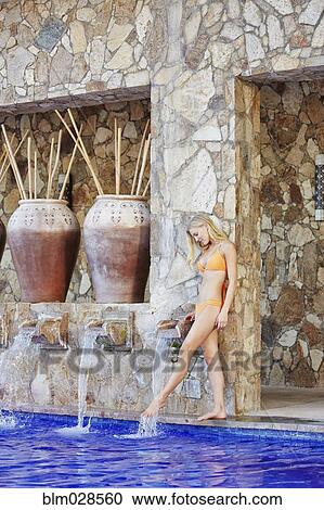 Stock Image - Caucasian woman dipping foot in swimming pool. Fotosearch