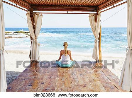 Stock Photo - Caucasian woman meditating in cabana overlooking ocean. Fotosearch