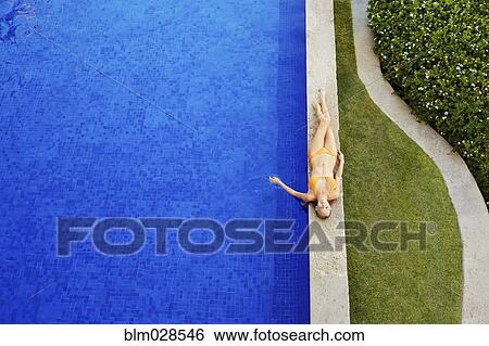 Stock Photograph - Caucasian woman relaxing by swimming pool. Fotosearch