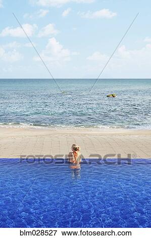 Stock Photo - Caucasian woman relaxing in infinity pool. Fotosearch