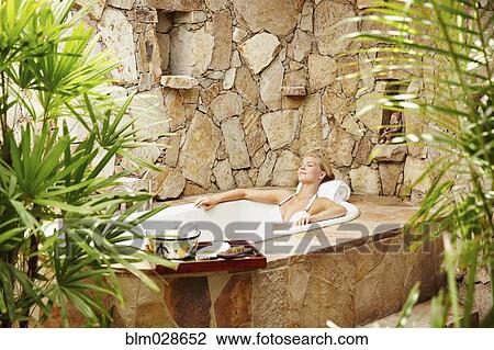 Stock Image - Caucasian woman relaxing in outdoor soaking tub. Fotosearch