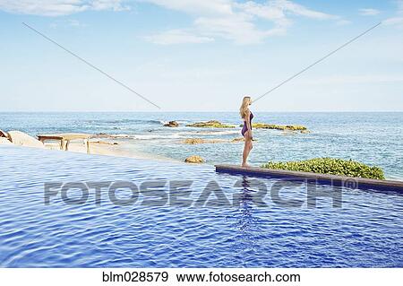 Stock Photo - Caucasian woman standing at the edge of infinity pool. Fotosearch