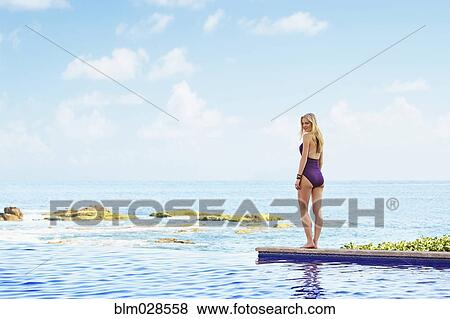 Stock Photo - Caucasian woman walking by infinity pool. Fotosearch