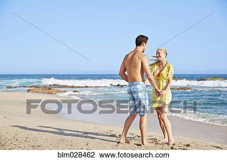 Stock Image - Couple holding hands on beach. Fotosearch