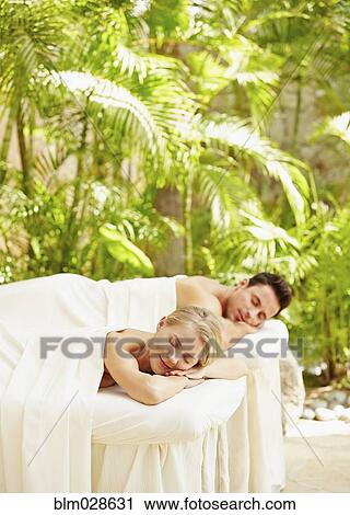 Stock Image - Couple laying on massage tables outdoors. Fotosearch